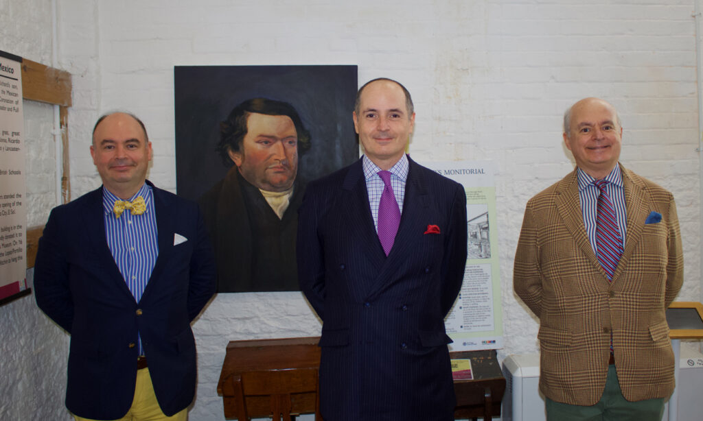 L-R Francisco, Ricardo and Rodrigo Lancaster-Jones stand before a portrait of Joseph Lancaster at the British Schools Museum